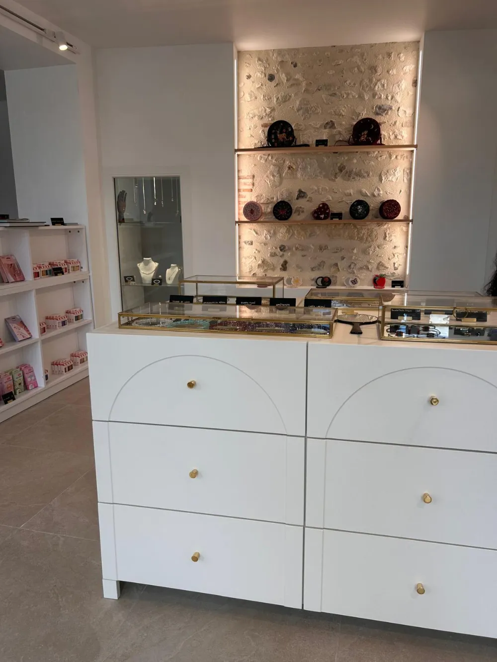 Intérieur de la boutique : comptoir blanc, vitrines de pierres et mur en pierre éclairé